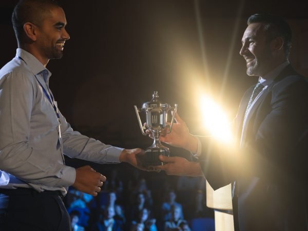 Side view of Caucasian businessman giving trophy to mixed race business male executive on stage in auditorium